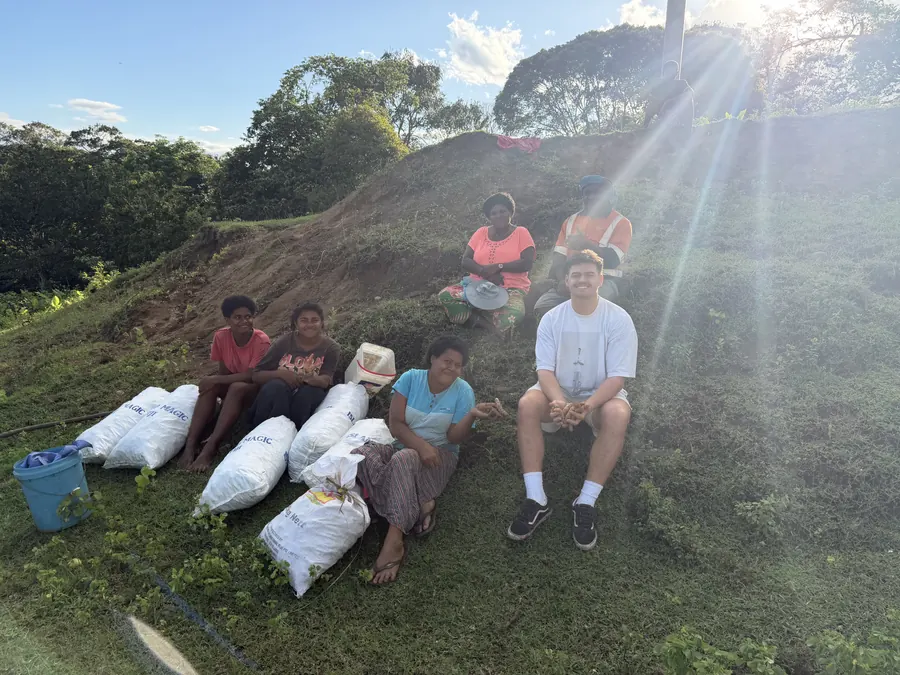 Blake with a family on a hillside in Fiji, harvest bags beside them